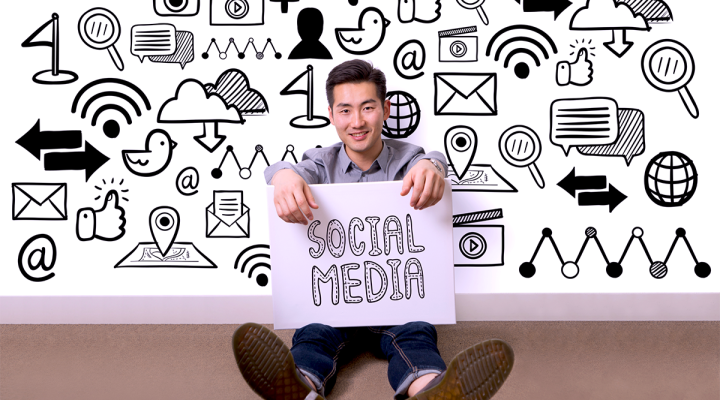 Small Business Owner Sitting In Front of a Social Media Icon Wall Holding a Sign